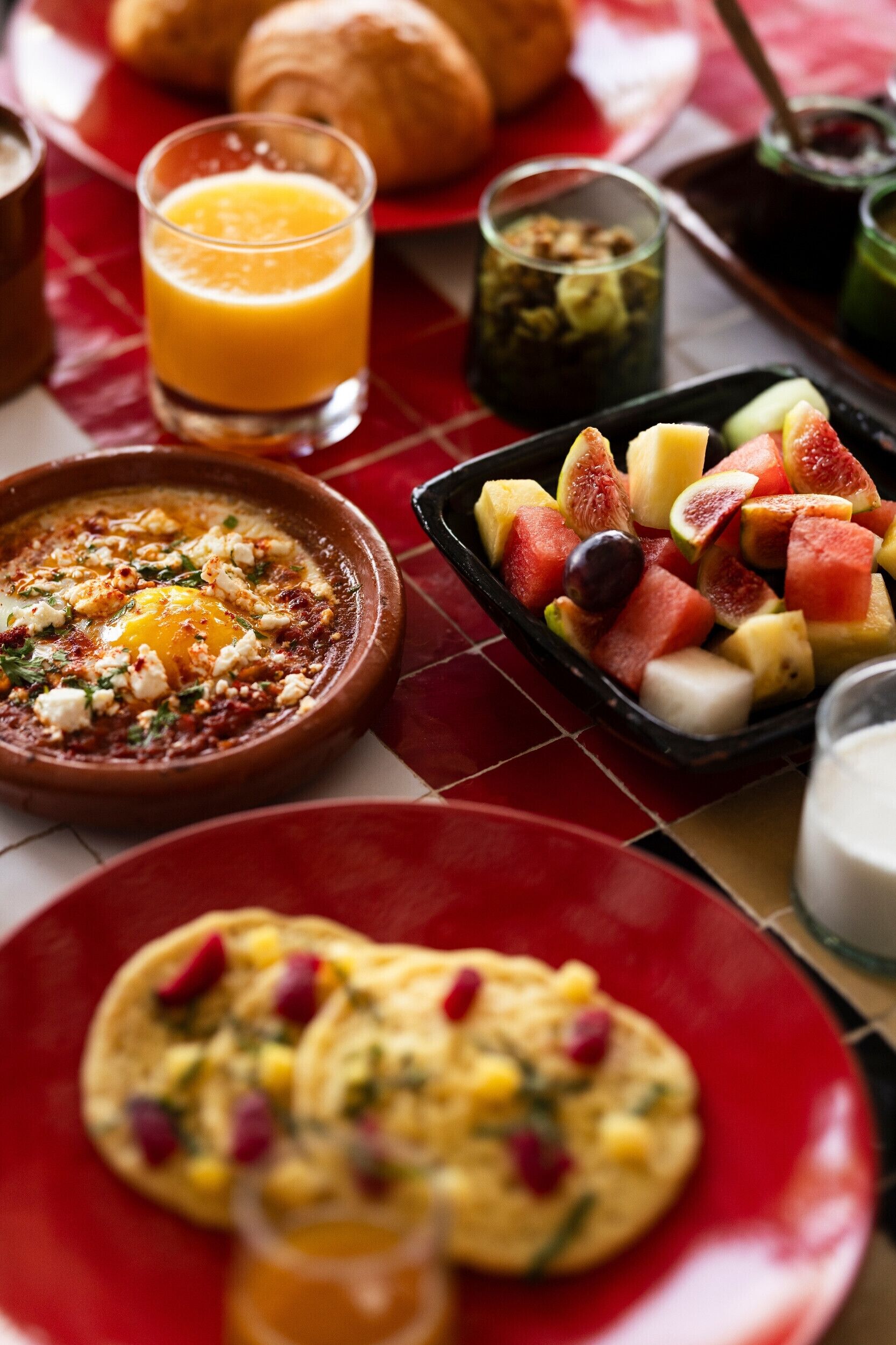Un desayuno con diversas opciones, incluyendo un tazón de huevos, una fuente de fruta y un vaso de jugo de naranja.