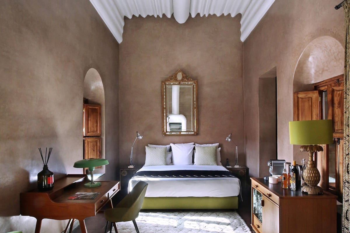 A bedroom with a bed, bedside tables, a desk, a chair, and a mirror.