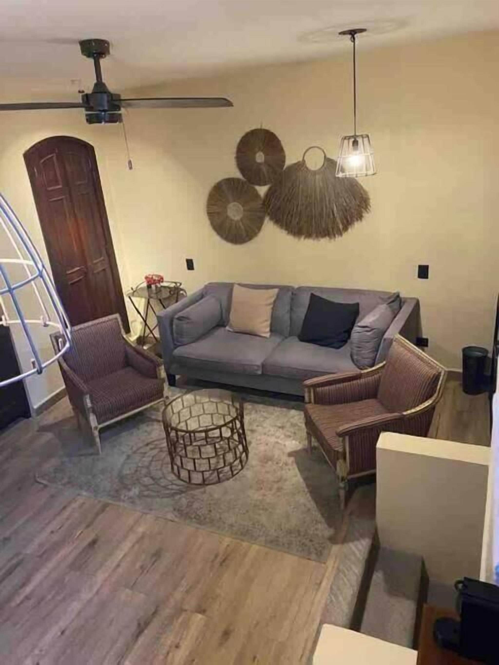 Una sala de estar con un sofá gris, dos sillones, una mesa de centro y un ventilador de techo.