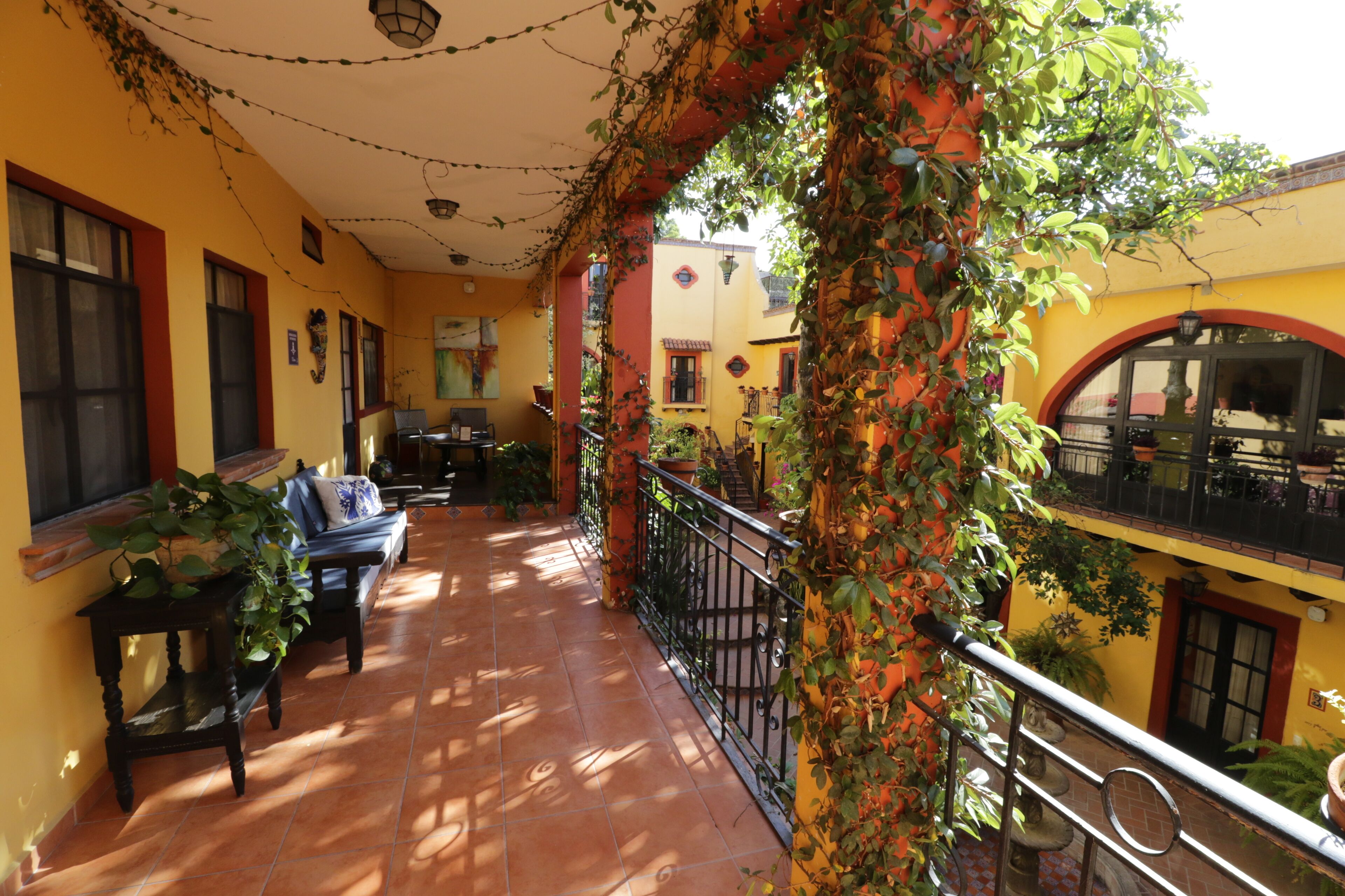 Un balcon ensoleillé avec un sol carrelé, une rambarde en métal noir et des plantes en pot.