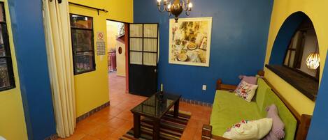 A room with a green sofa, a small table, a chandelier, and a colorful wall mural.