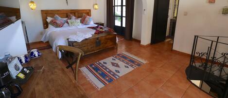 A bedroom with a wooden bed, a ceiling fan, a window with curtains, a wooden desk, and a patterned rug.