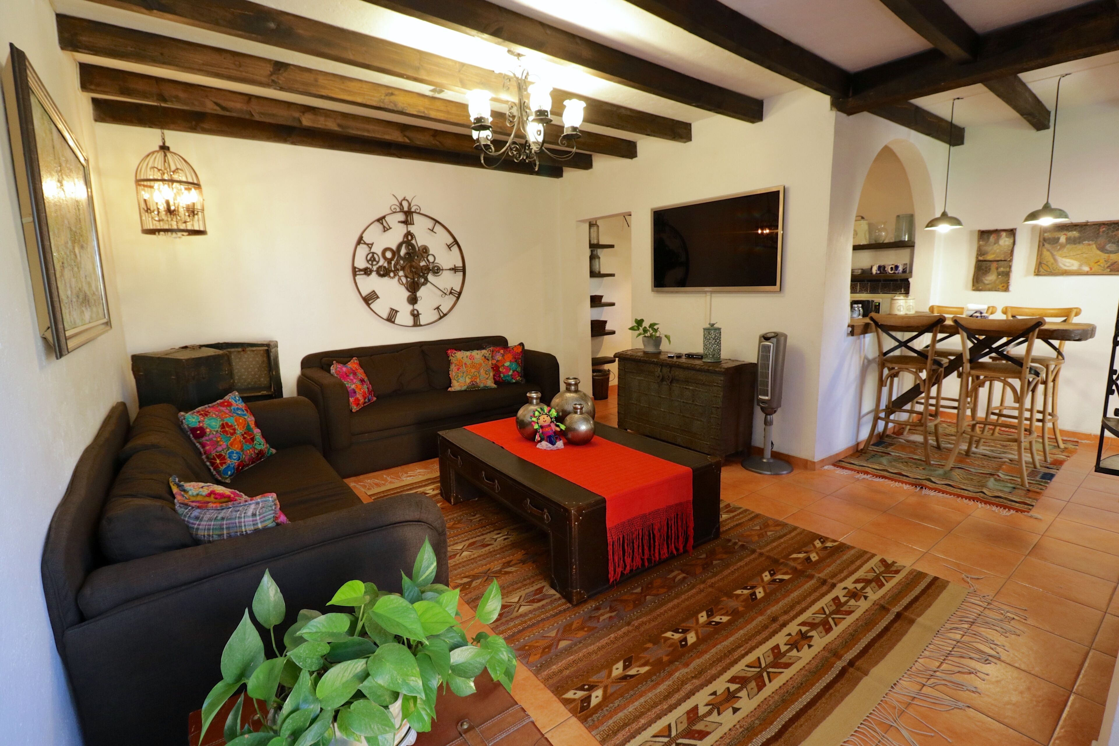 A living room with a sofa, a coffee table, and a TV. There is a dining area with a table and chairs.