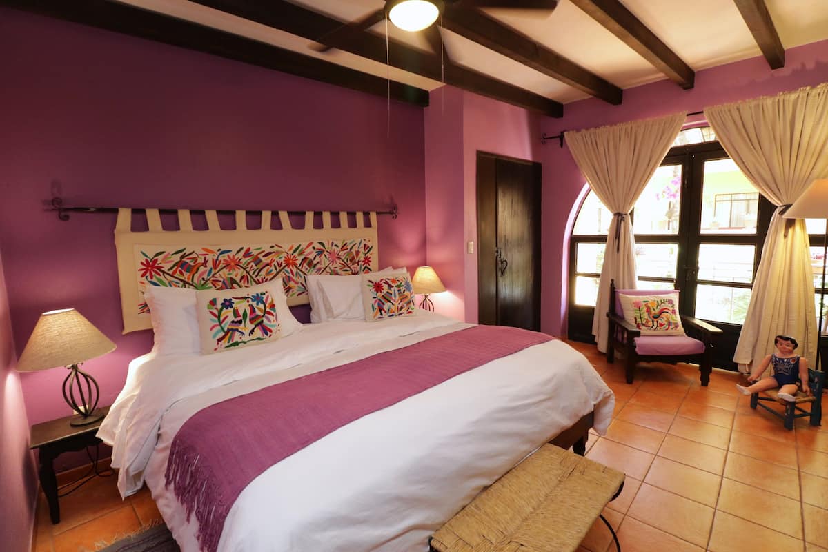 Une chambre avec un grand lit, une chaise, une table et une fenêtre avec des rideaux.