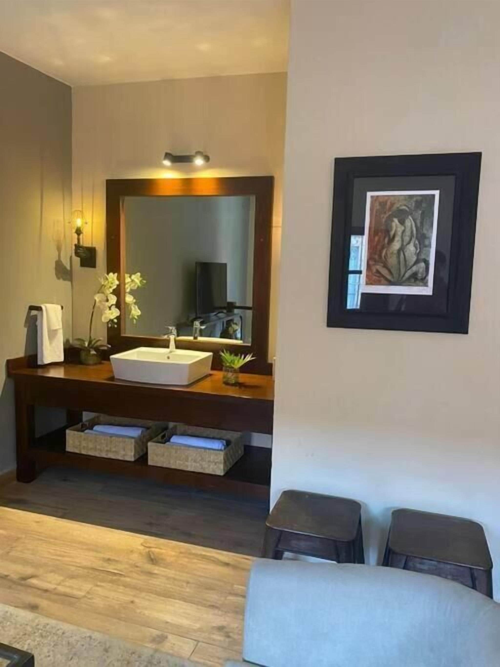 A modern bathroom with a large mirror, a white sink, and a framed artwork on the wall.