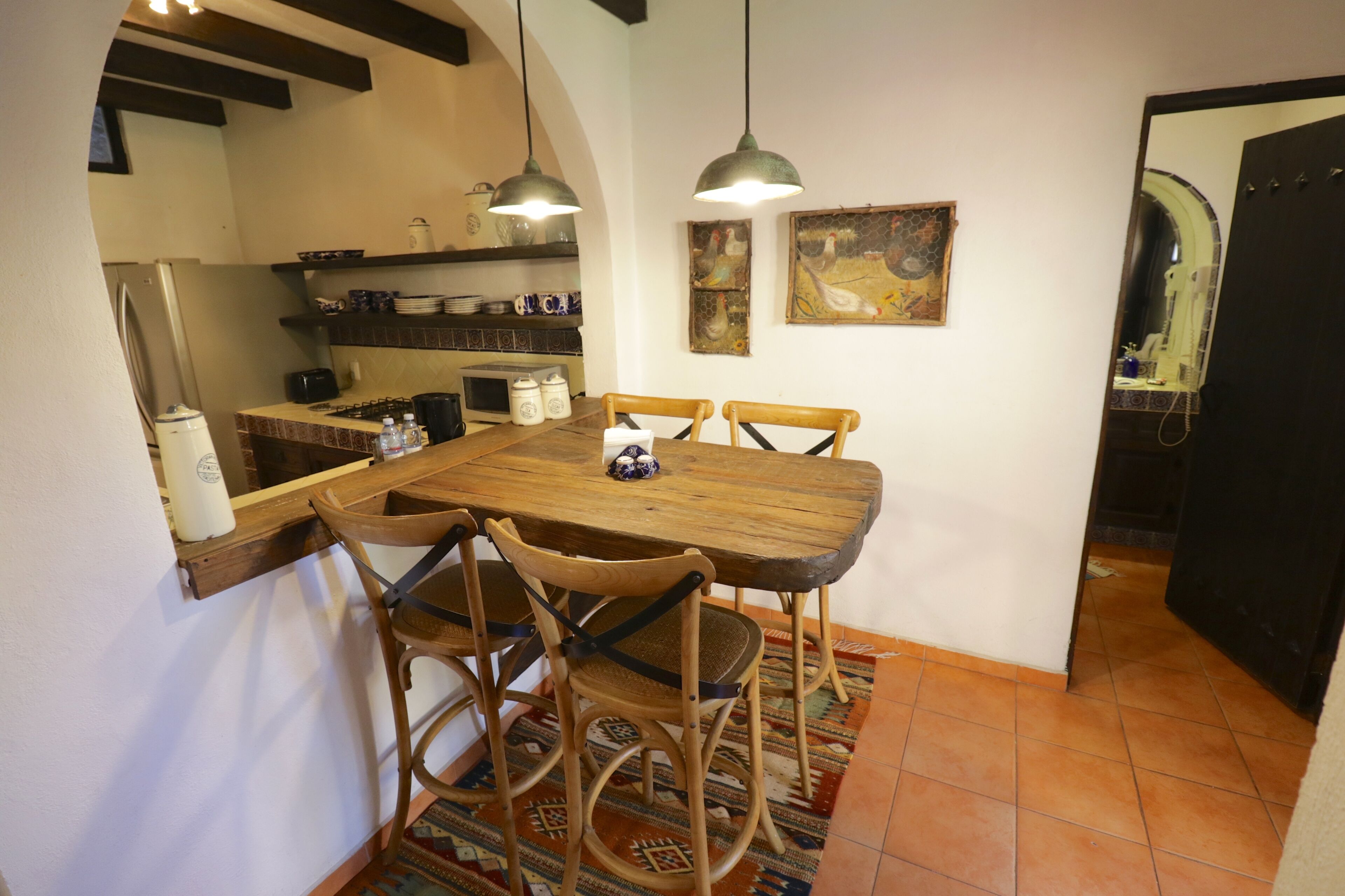 A dining area with a wooden table and chairs, a tiled floor, and hanging pendant lights.