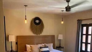 Ein Schlafzimmer mit einem großen Bett, zwei Nachttischen, einer Wanddekoration und einem Deckenventilator.
