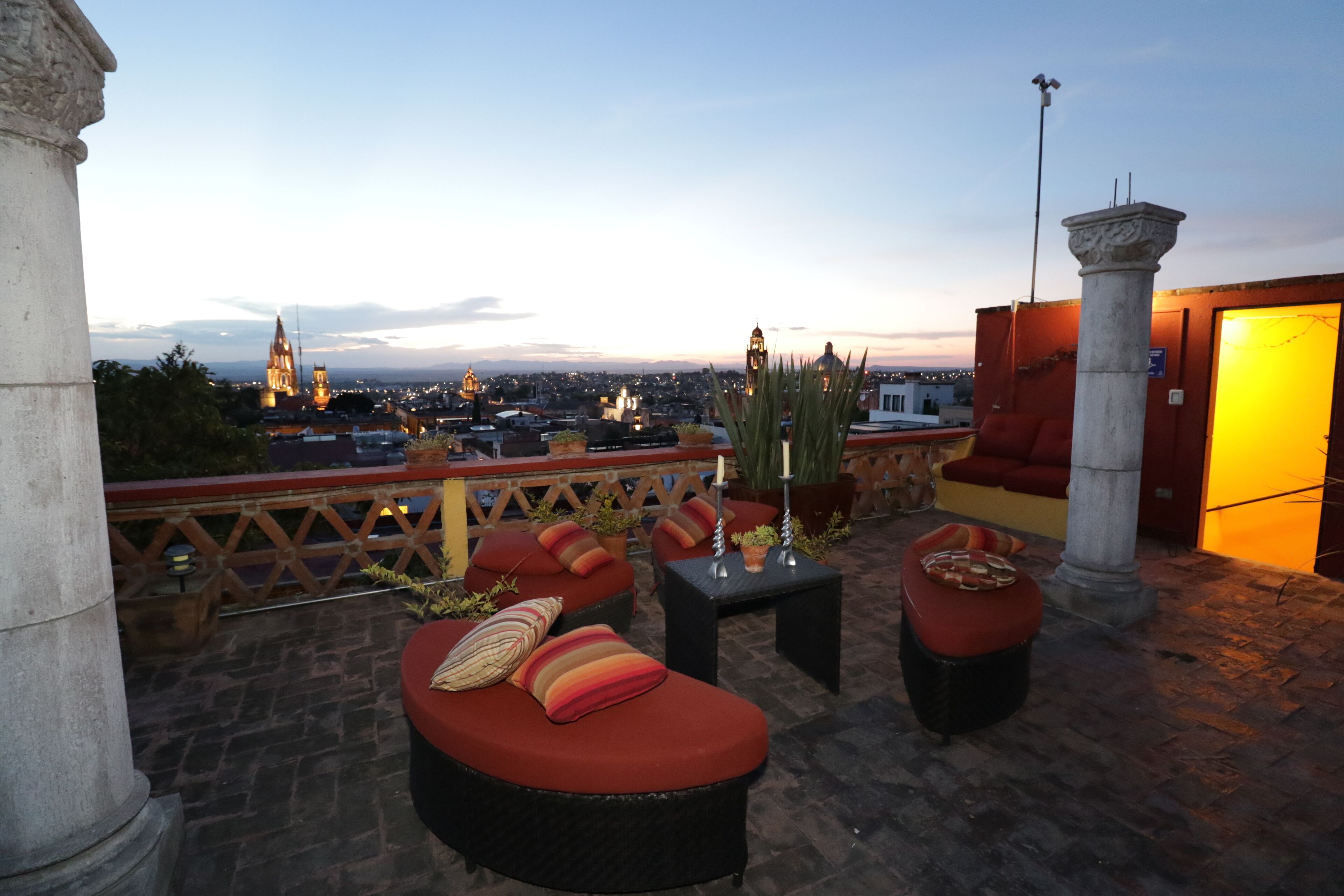 A rooftop terrace with outdoor seating, a view of the cityscape, and a stone column structure.