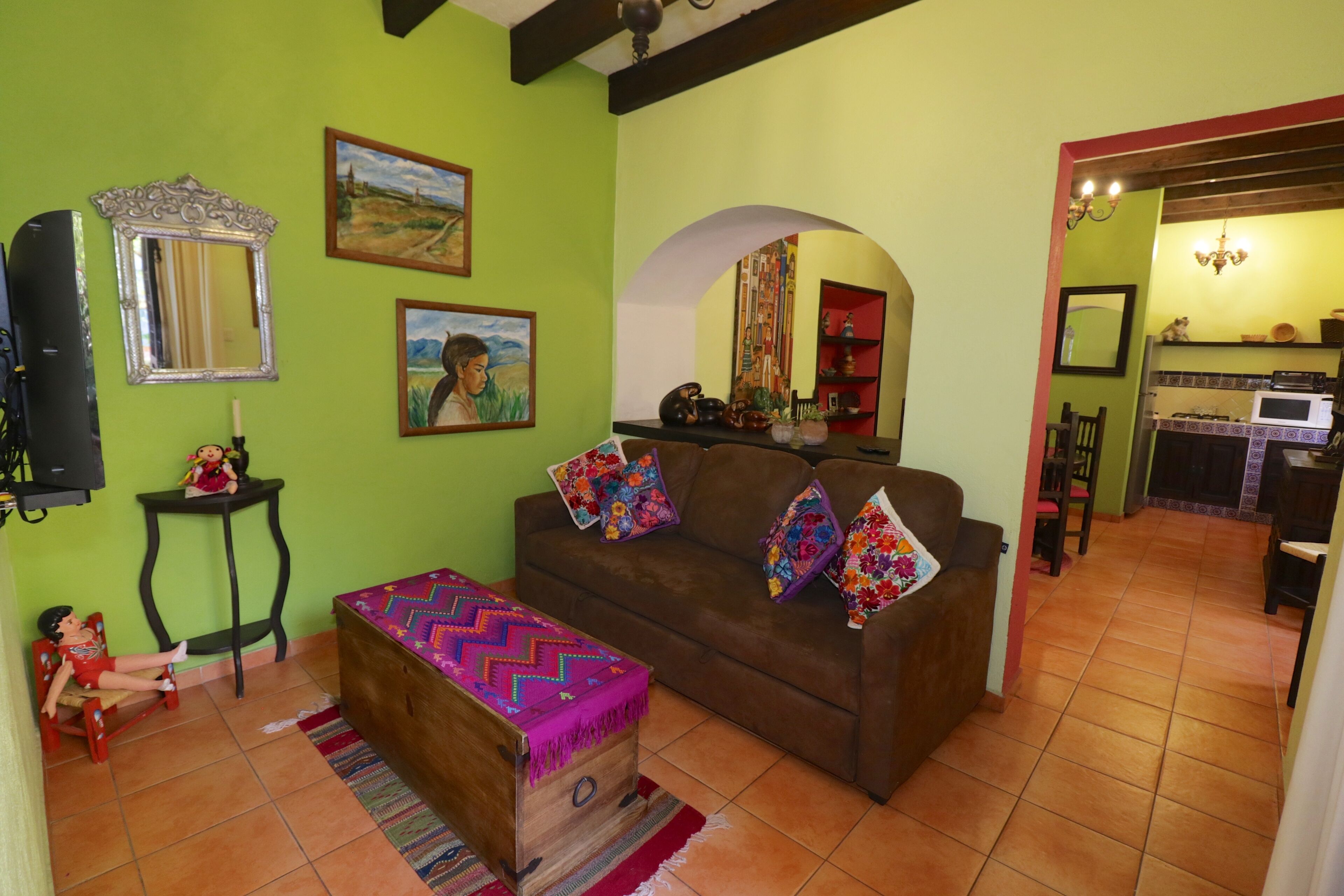 Una sala acogedora con un sofá marrón, cojines coloridos, un cofre de madera y una mesita con una muñeca.