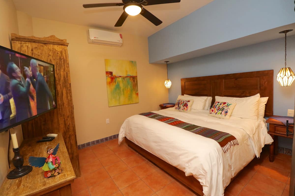 Une chambre à coucher comprenant un lit, un téléviseur, un ventilateur de plafond et un climatiseur fixé au mur.