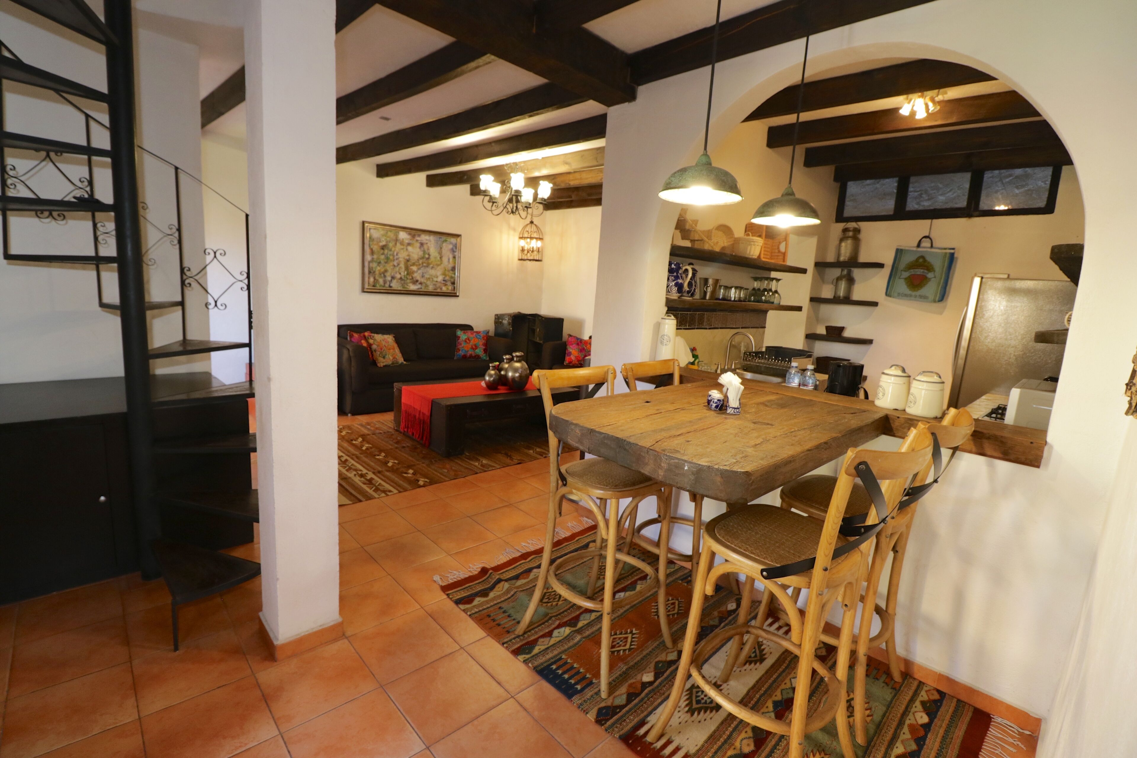 Un espacio acogedor con mesa y sillas de madera, un sofá y una escalera.