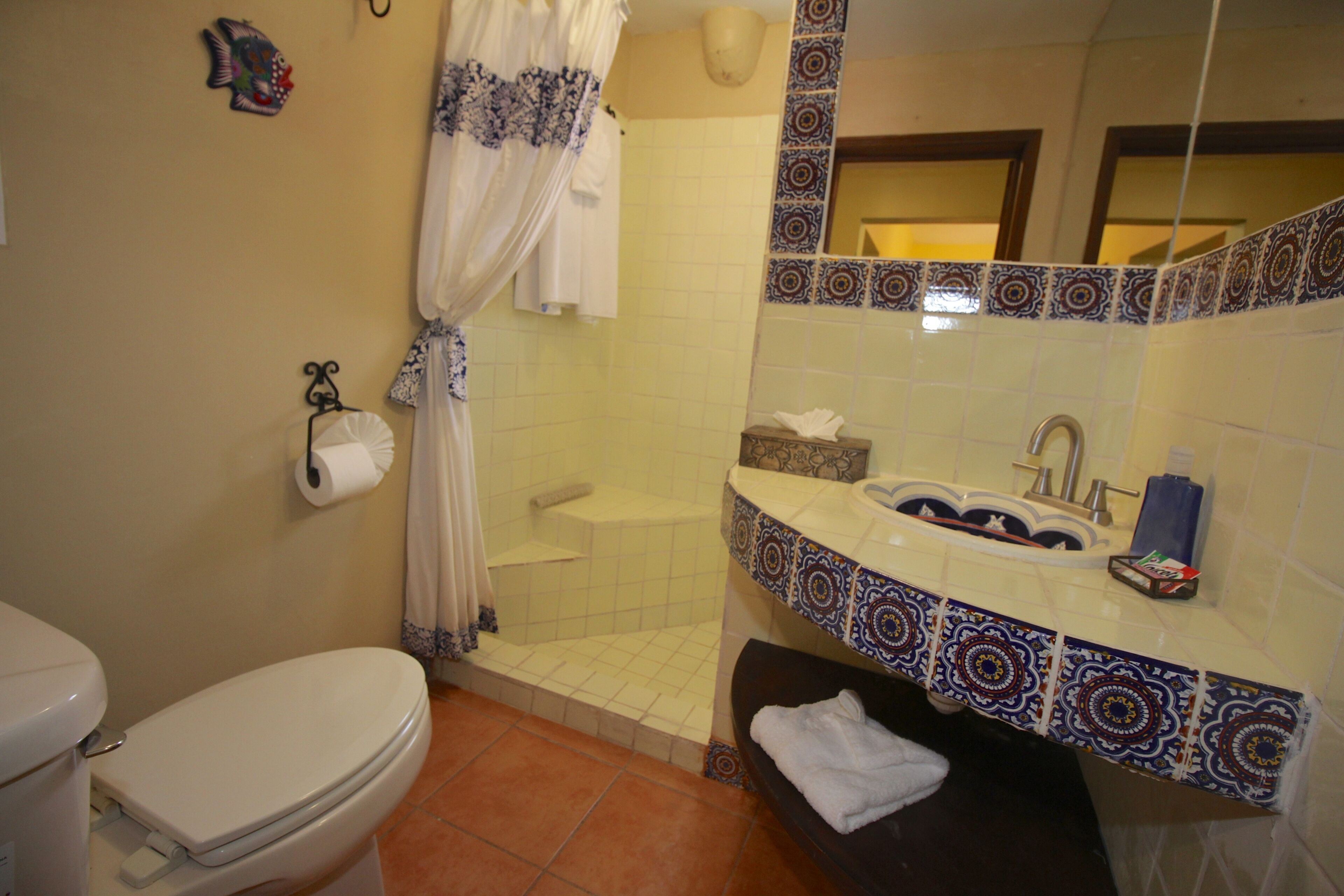 A bathroom with a toilet, shower, sink, and a mirror.