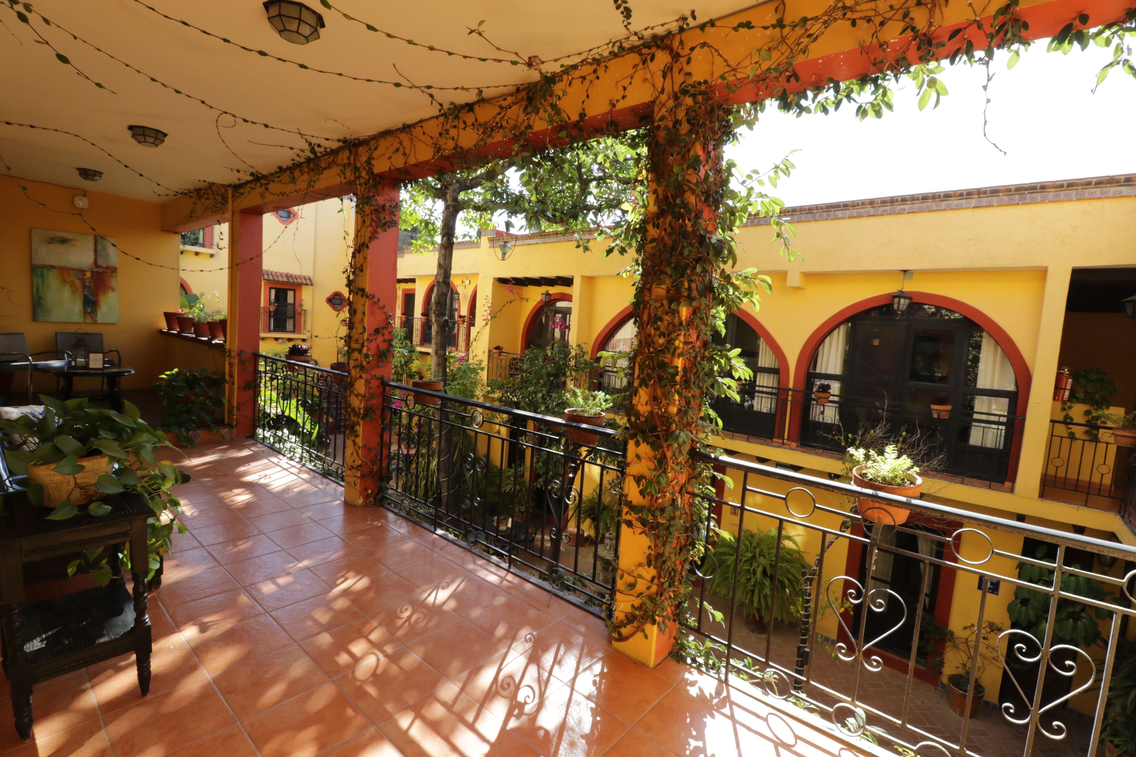 A covered outdoor area with tiled flooring, potted plants, and a metal railing.