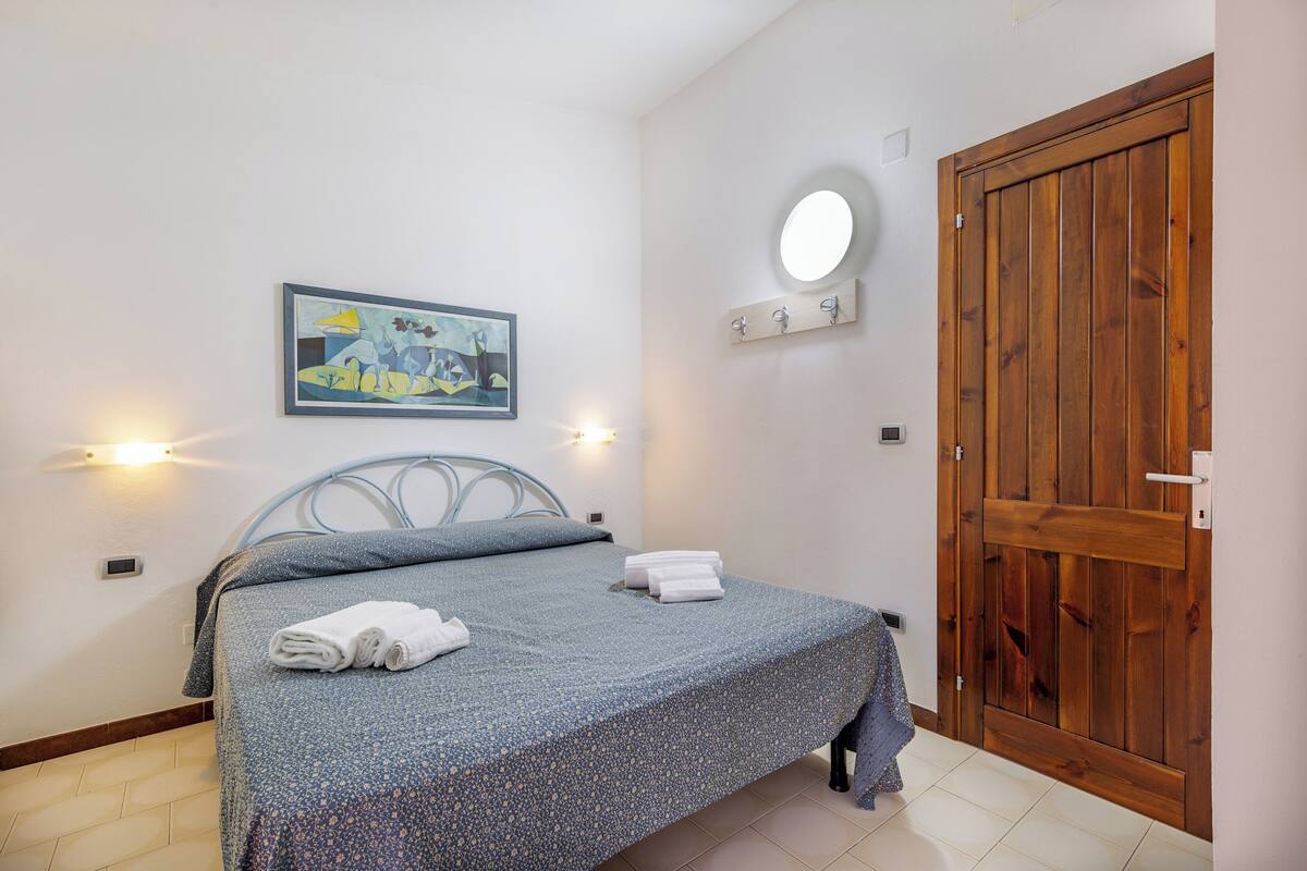 Una camera da letto con un letto, un quadro, una lampada a parete, una porta in legno e un piccolo ripiano con ganci.
