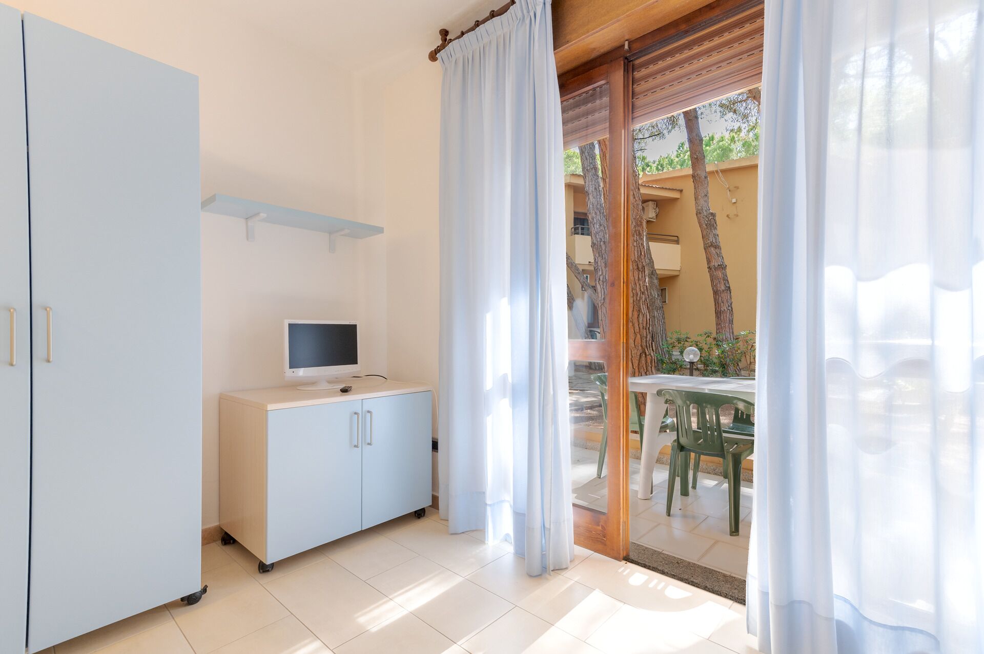 Ein Zimmer mit einem weißen Schrank, einem Flachbildfernseher und einer Glastür, die auf einen Außenbereich mit Tisch und Stühlen führt.