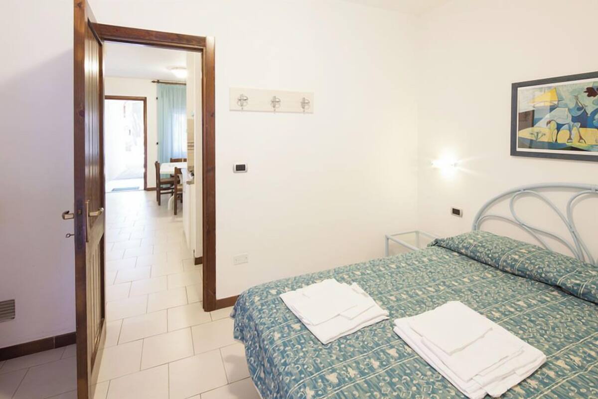 Una camera da letto con un letto, una porta che dà su un'area pranzo e un punto luce fissato al muro.