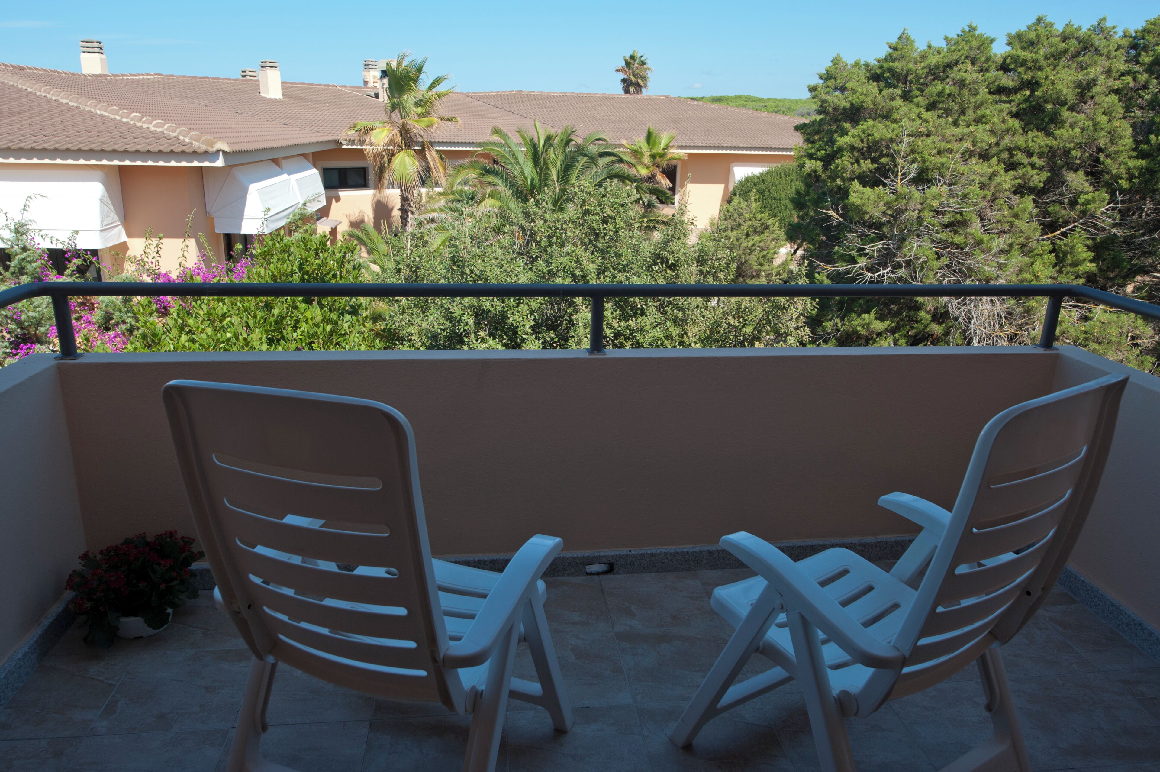 Ein Balkon mit zwei weißen Stühlen, einem Geländer und Blick auf Häuser und Bäume.