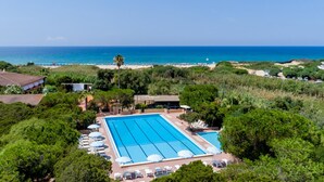 Ein großer Pool mit Liegestühlen und Sonnenschirmen, umgeben von Grün und mit Blick auf einen Strand und den Ozean.