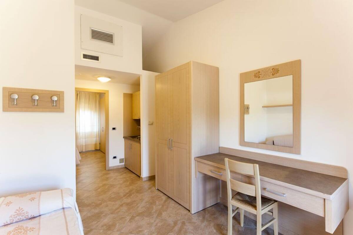 Una camera da letto con una scrivania in legno, una sedia, un armadio e uno specchio.