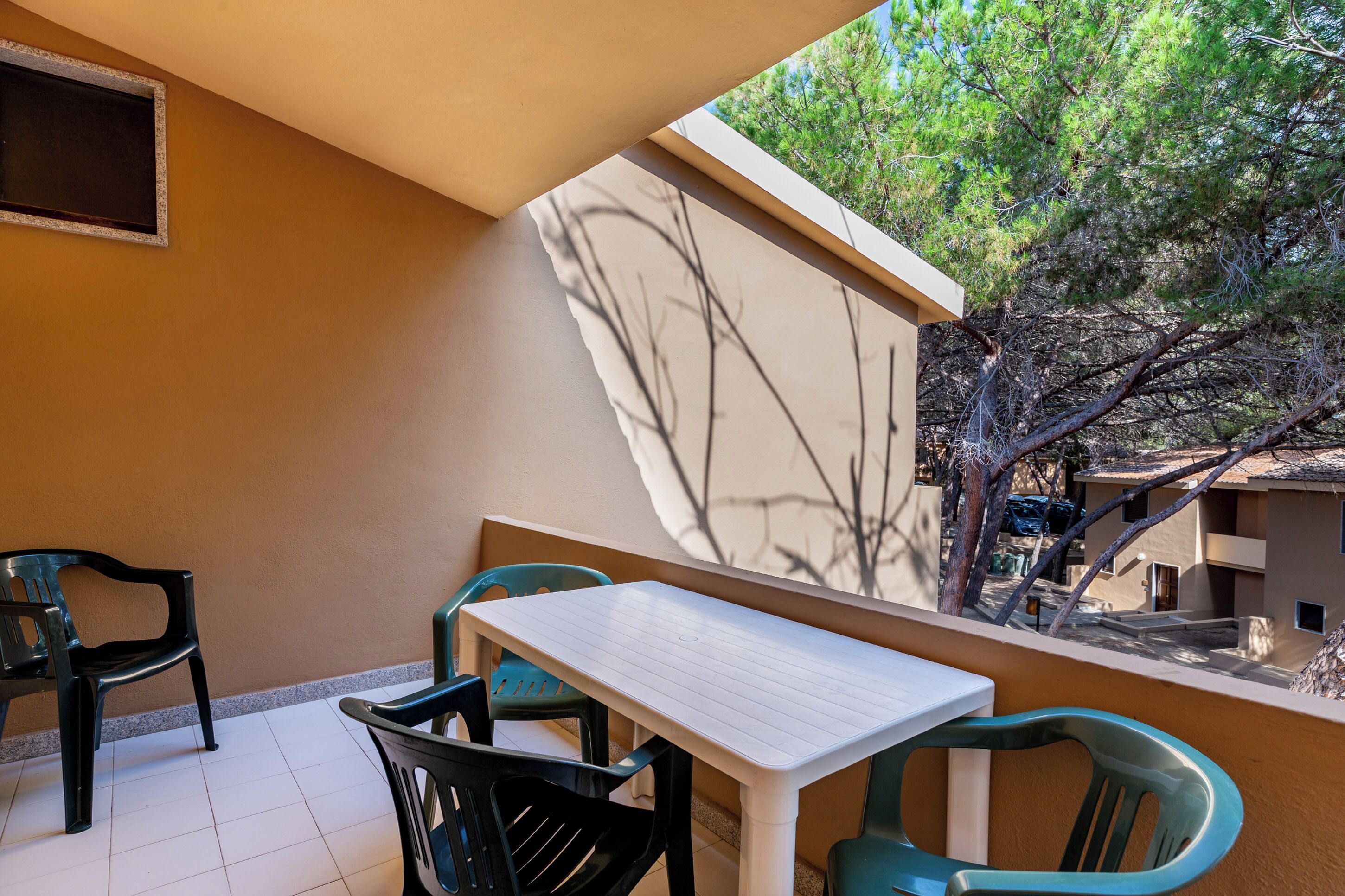 Ein Balkon mit weißem Tisch und Stühlen, Blick auf Bäume und ein Gebäude im Hintergrund.