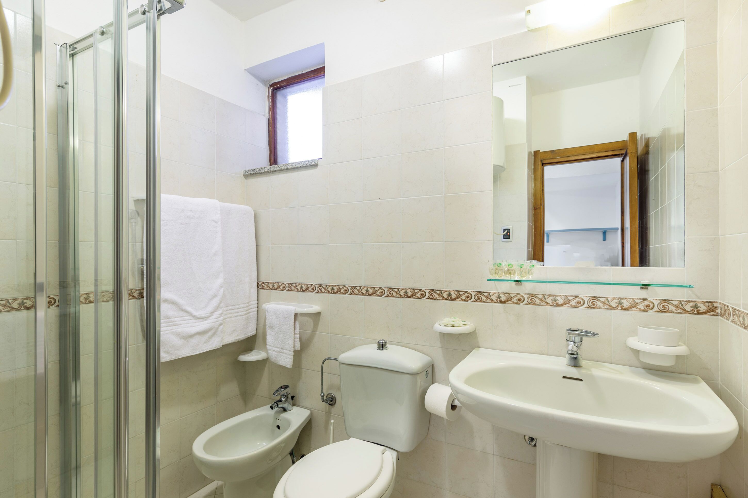 Une salle de bain avec une douche à parois de verre, des toilettes, un bidet, un lavabo et un miroir.