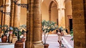 An architectural space with arches and columns, potted plants, and a person walking. - Le Casette di Lù (Agrigento)