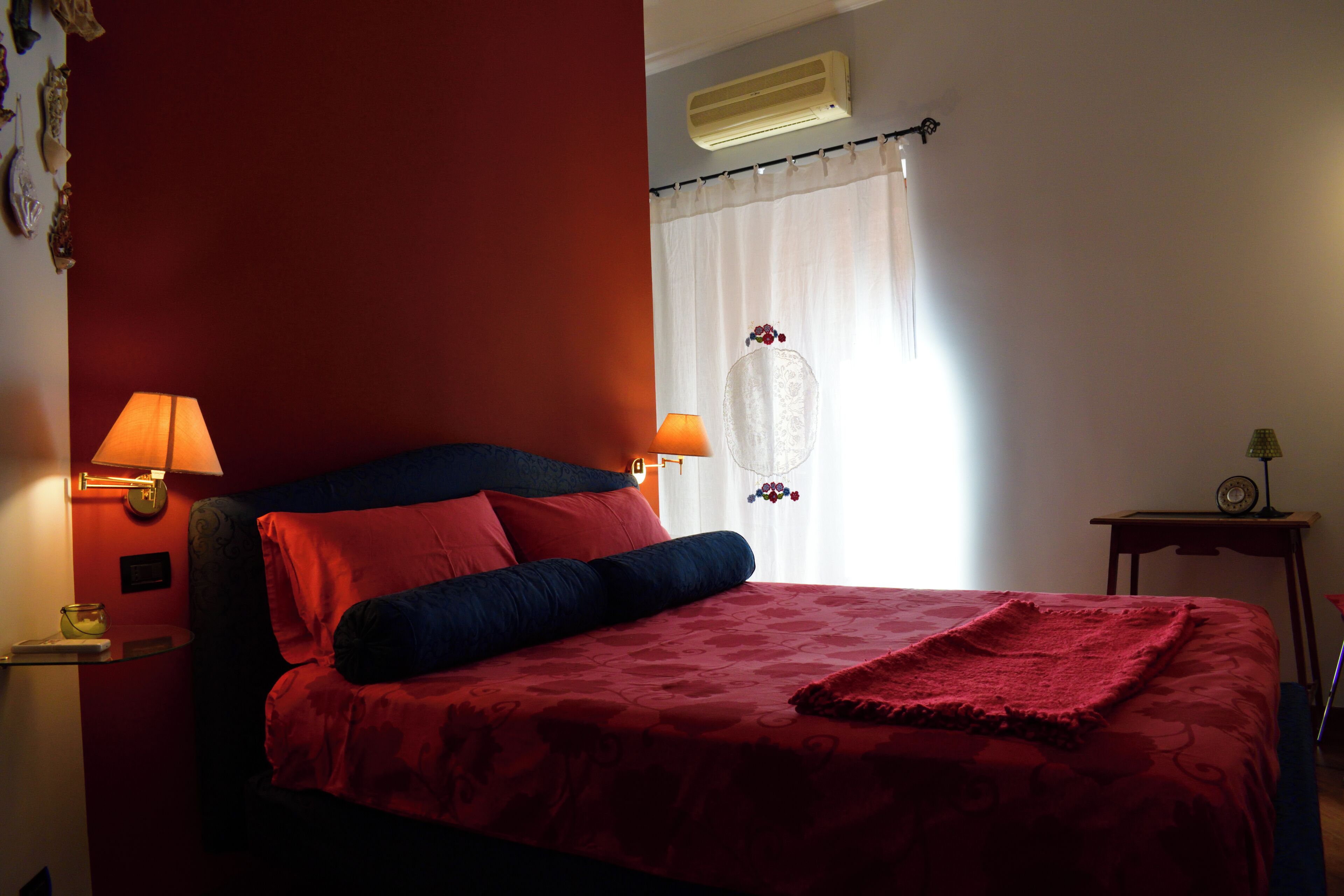 Un dormitorio con cama, dos lámparas de noche, una mesita de noche, aire acondicionado de pared y una ventana con cortinas.
