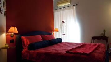 Un dormitorio con cama, dos lámparas de noche, una mesita de noche, aire acondicionado de pared y una ventana con cortinas.