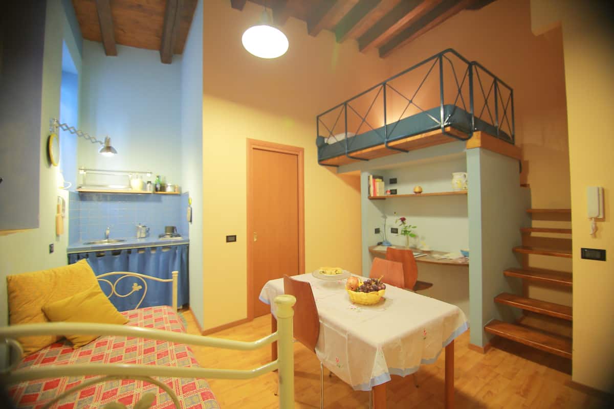 Ein Schlafzimmer mit Bett, einem Esstisch mit Obstkorb, einer Küchenzeile und einer Treppe.