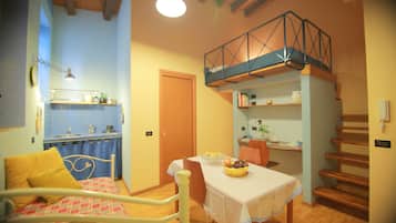 Un dormitorio con cama, una mesa de comedor con frutero, una zona de cocina y una escalera.