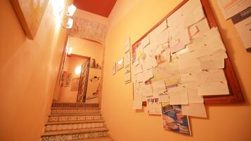 A hallway with a wooden staircase, a bulletin board with papers, and a brick wall.