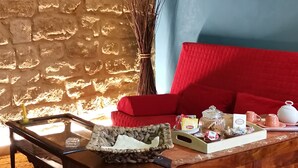 A room with a stone wall, a wooden cabinet with drawers, a red sofa, and a small table with a tray of items. - Le Casette di Lù (Agrigento)