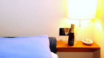 A hotel room with a bed, a nightstand with a bottle of champagne, a glass, and a plate of food.