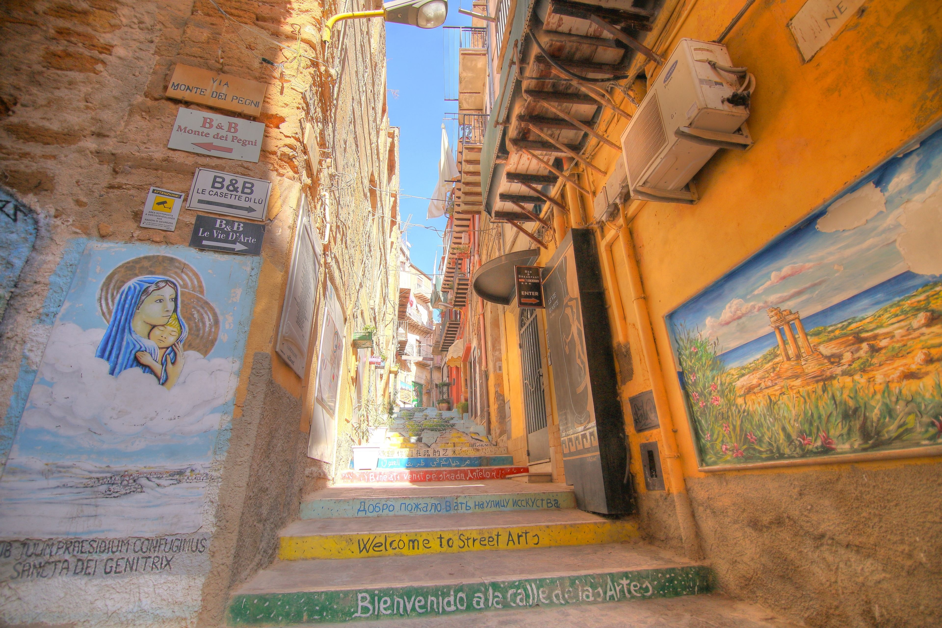 Une rue étroite ornée de peintures murales et d’enseignes colorées, dont une qui indique : « Bienvenue dans l’univers du street art ».