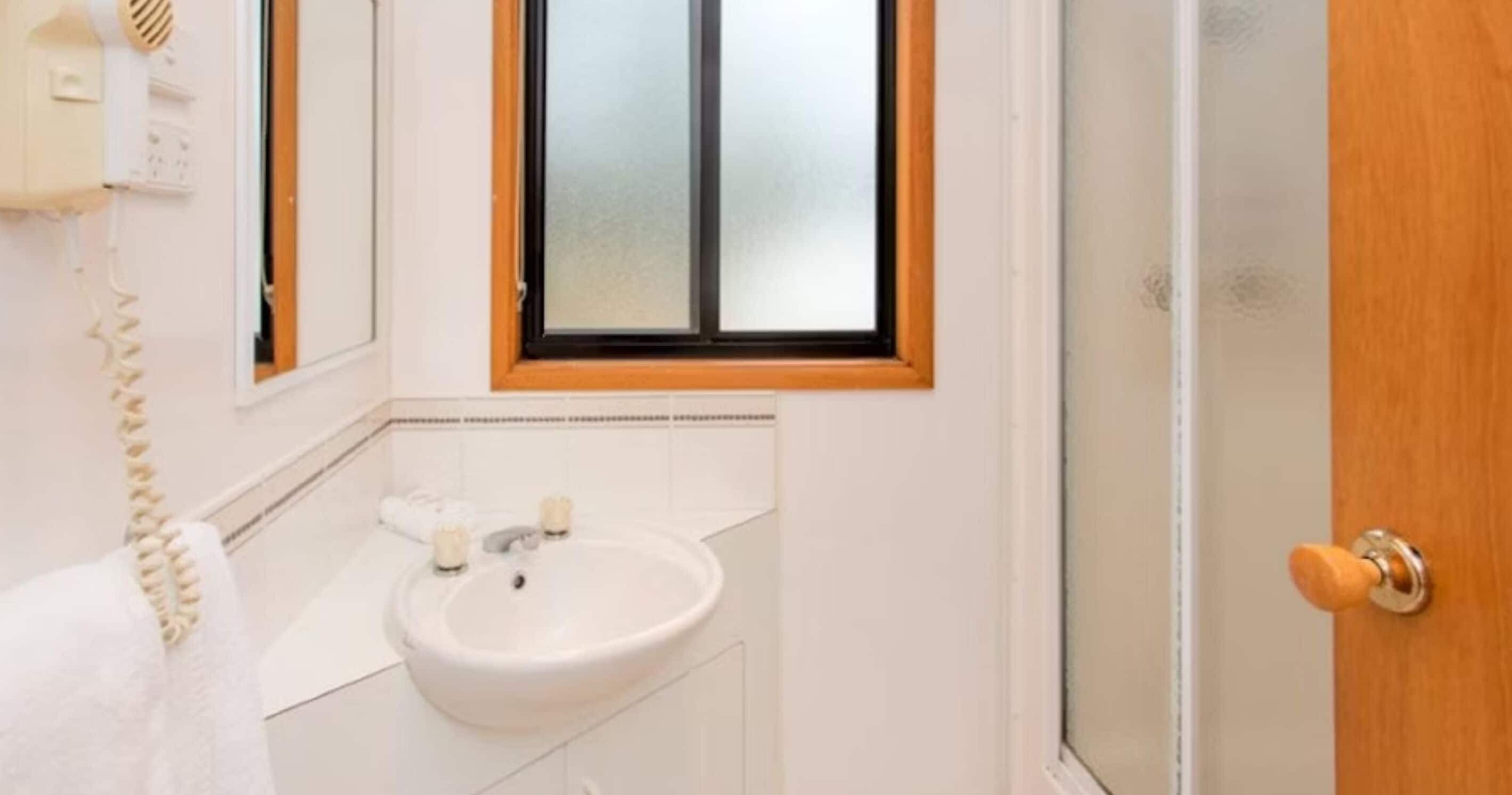 A bathroom with a white sink, a mirror, and a window with a wooden frame.