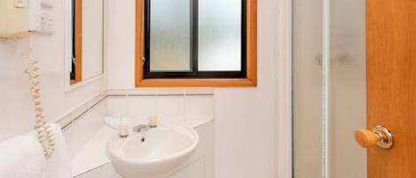 A bathroom with a white sink, a mirror, and a window with a wooden frame.