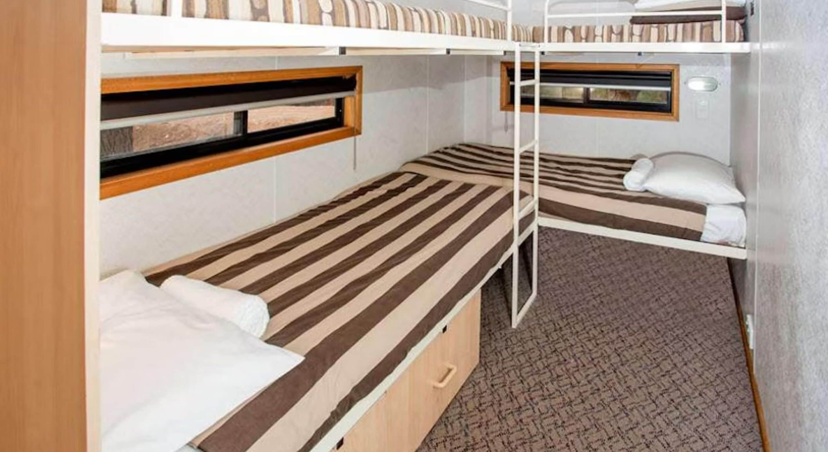 A compact, bunk-style room with two beds, each with a wooden headboard and a window.