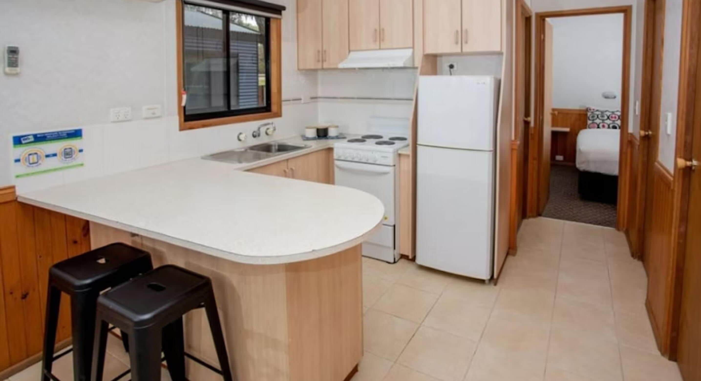 A compact kitchen with a white countertop, a stove, a refrigerator, and two bar stools.