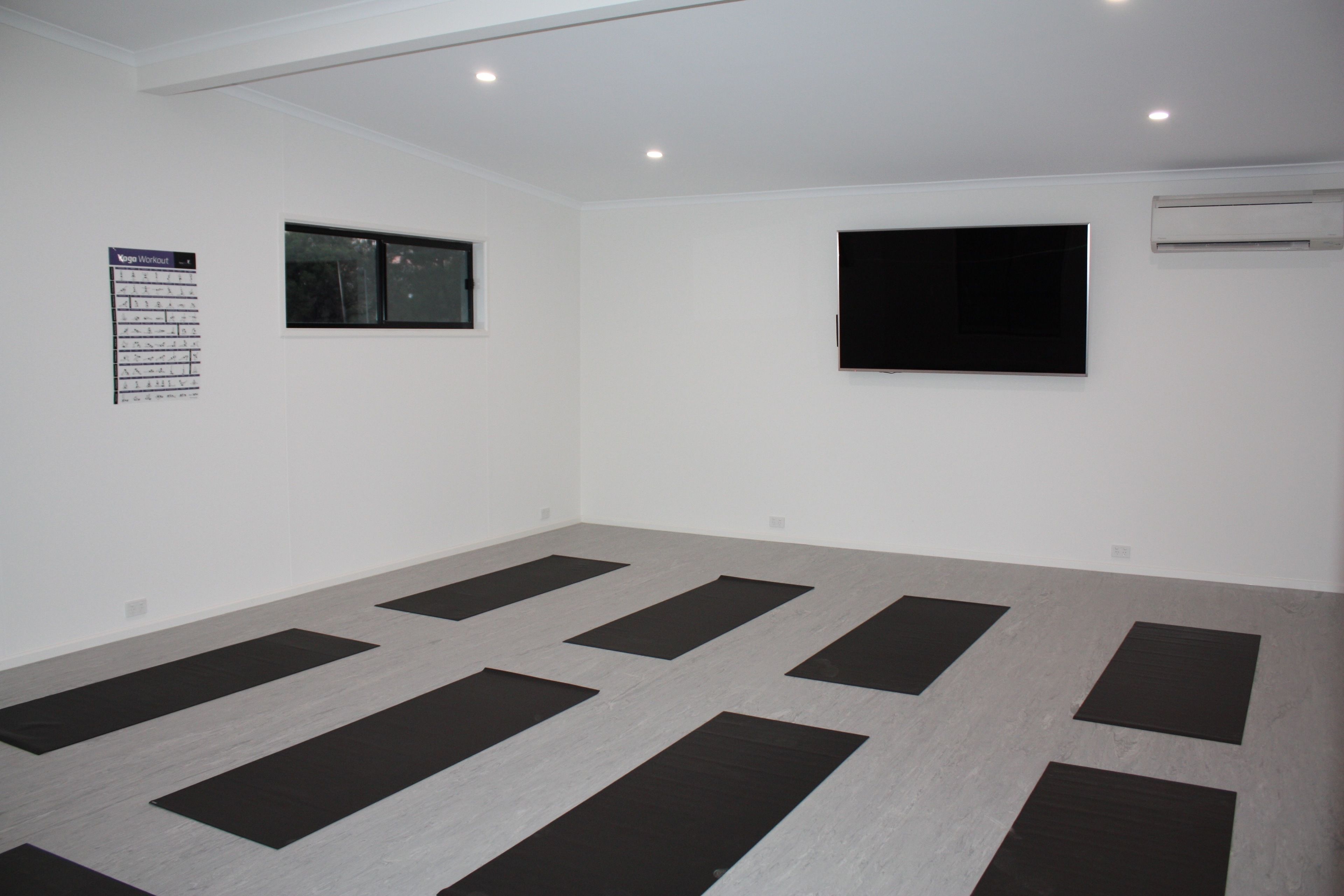 A spacious room with a large window, a mounted flat-screen TV, and a yoga mat layout on the floor.