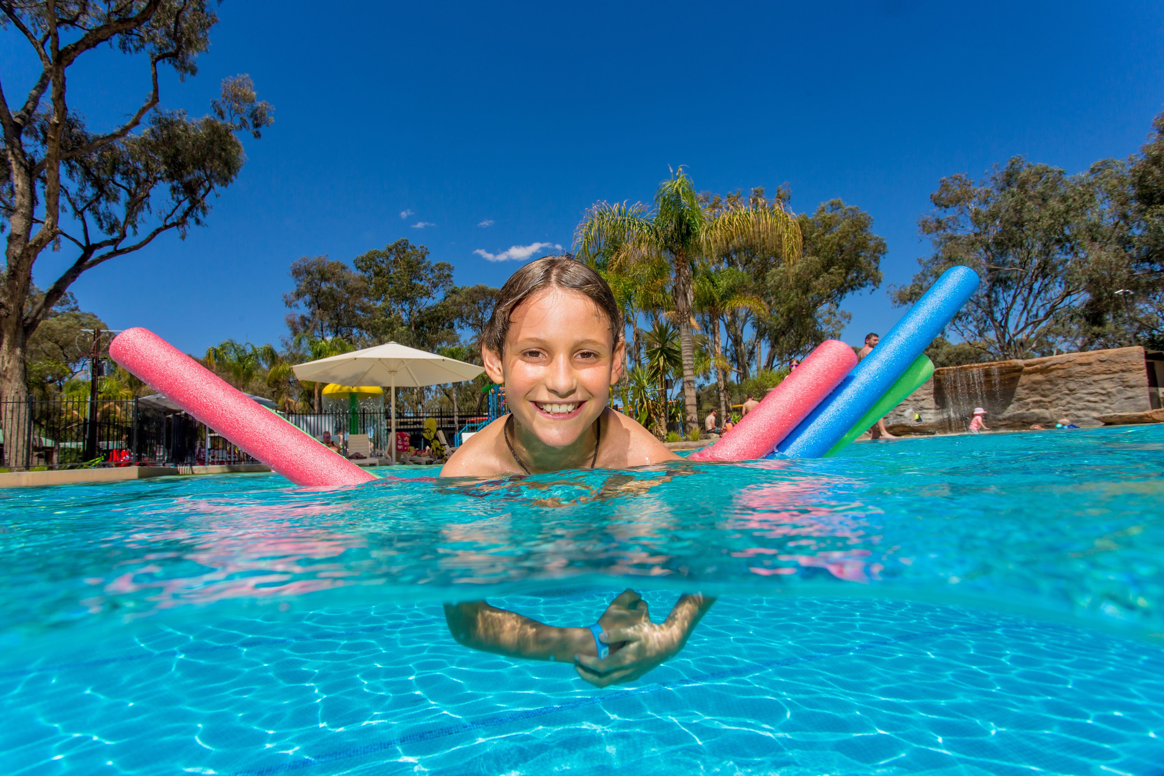 A pool with clear blue water, surrounded by trees and a sandy area.
