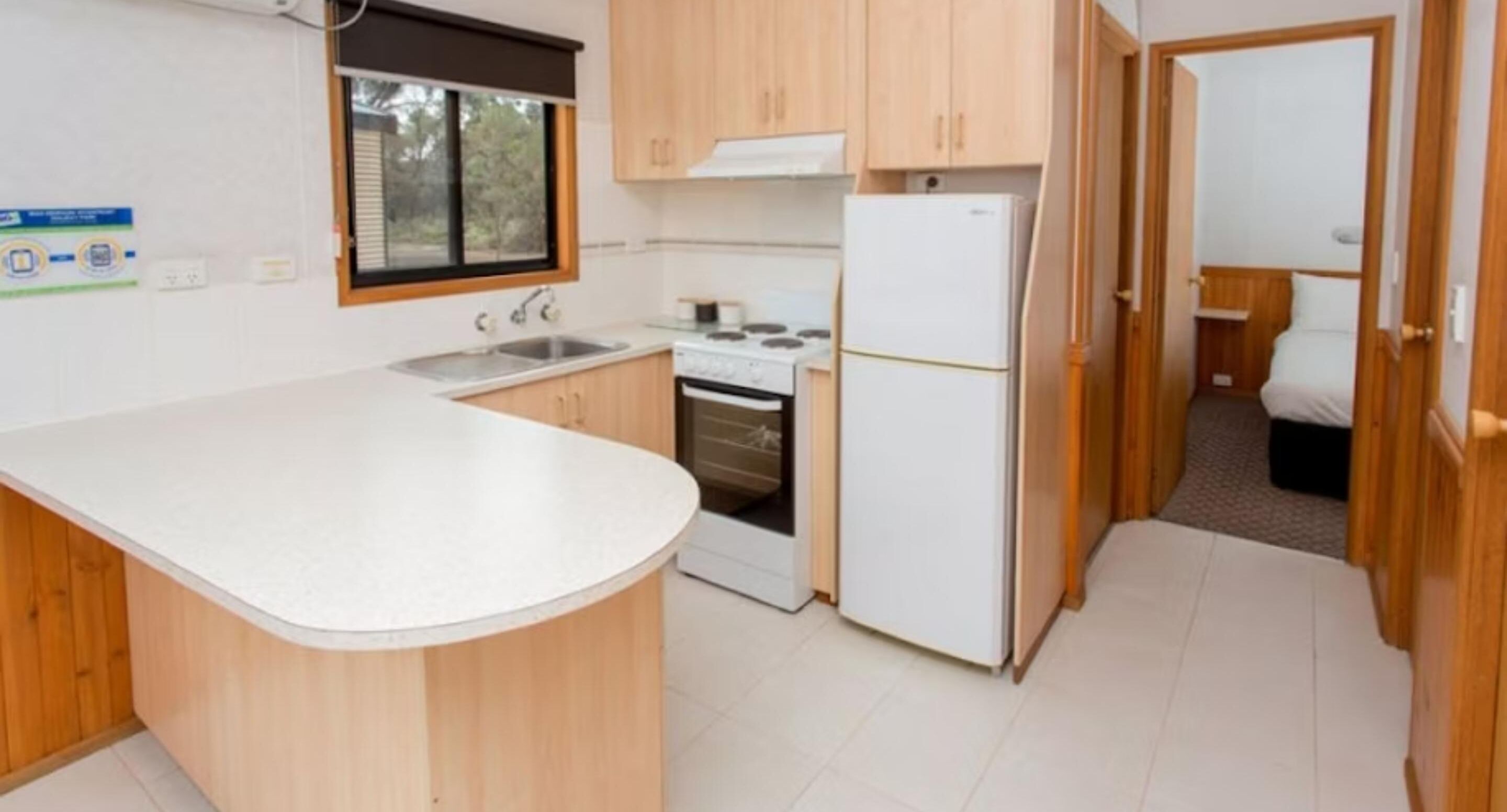 Cocina pequeña con gabinetes de madera, encimera blanca, estufa y refrigerador.