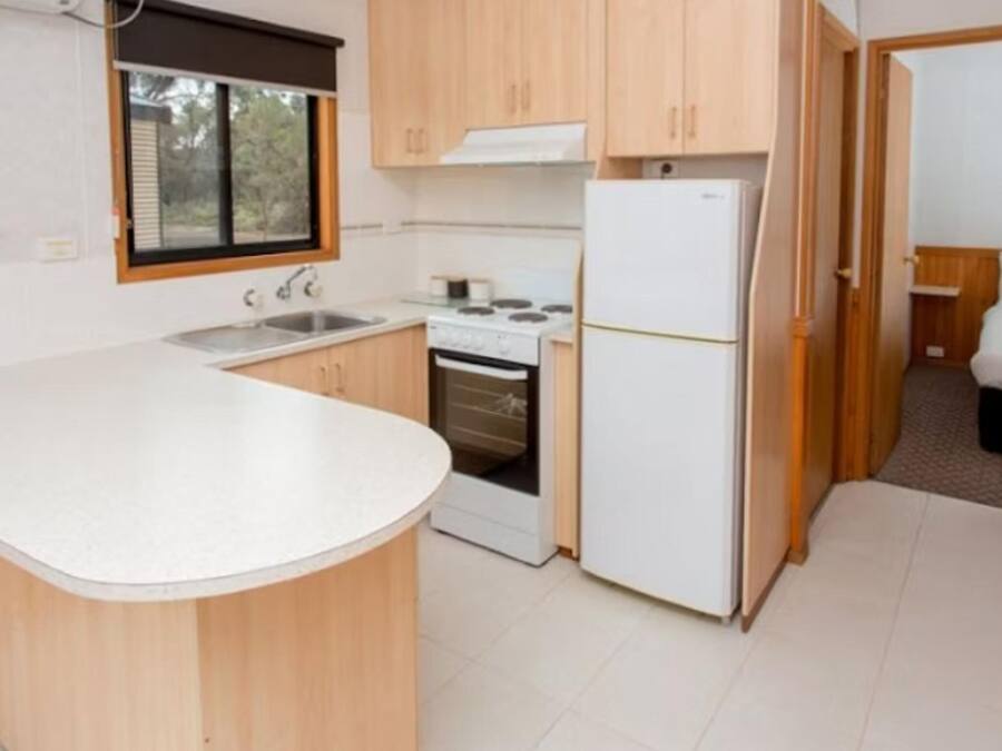 Cocina pequeña con gabinetes de madera, encimera blanca, estufa y refrigerador.