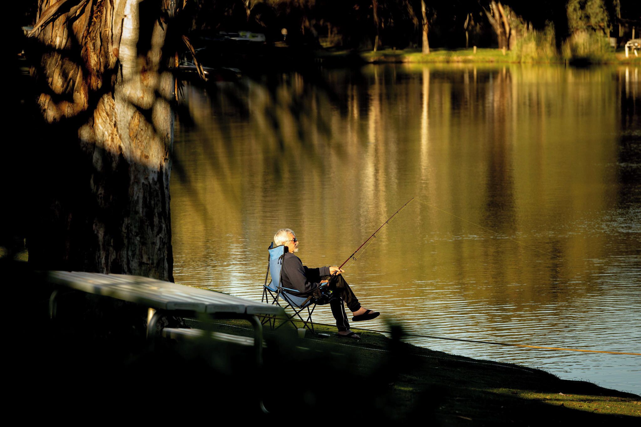 A person sitting on a chair by a calm lake, fishing.