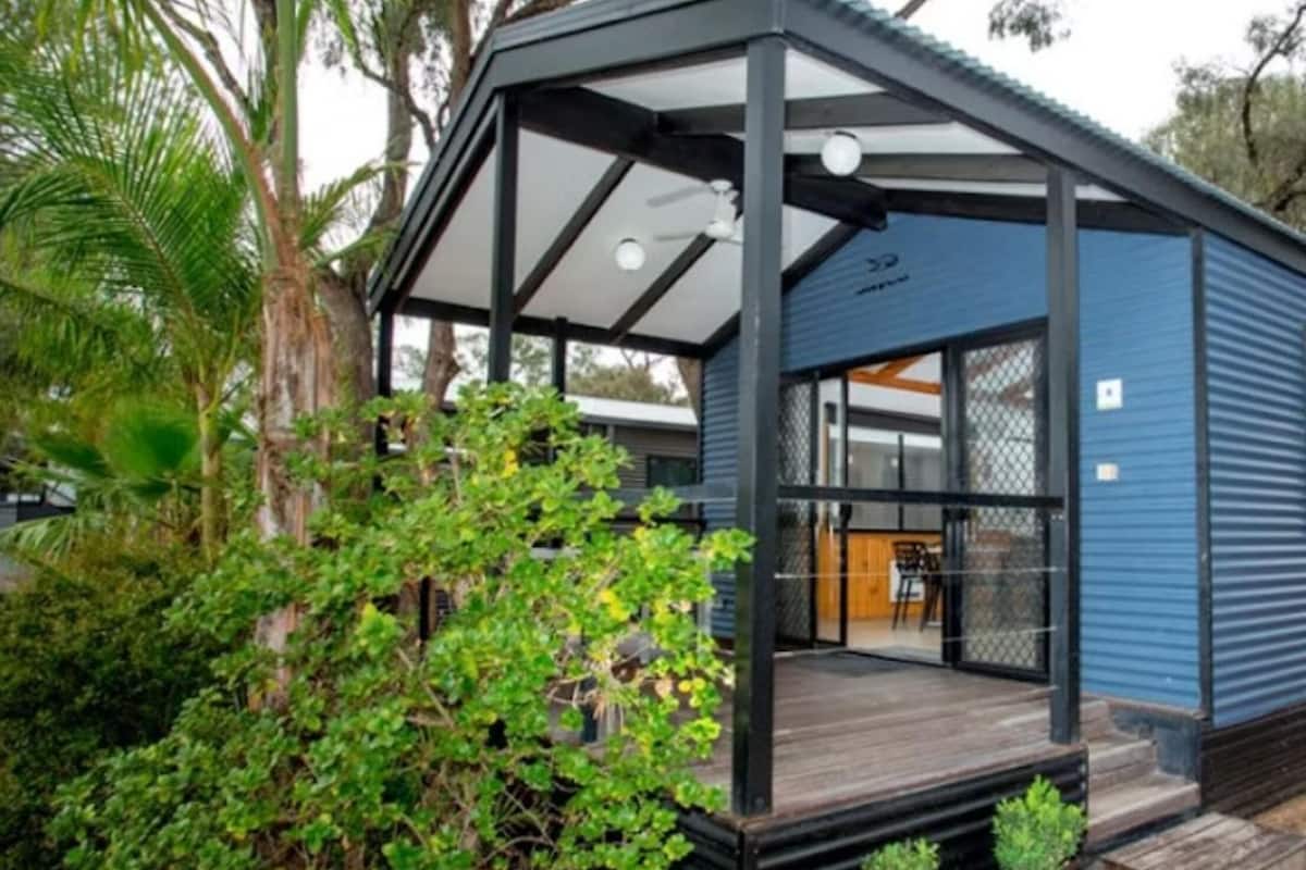 Una casa móvil moderna con porche cubierto, ventanas amplias y un área exterior cercada.
