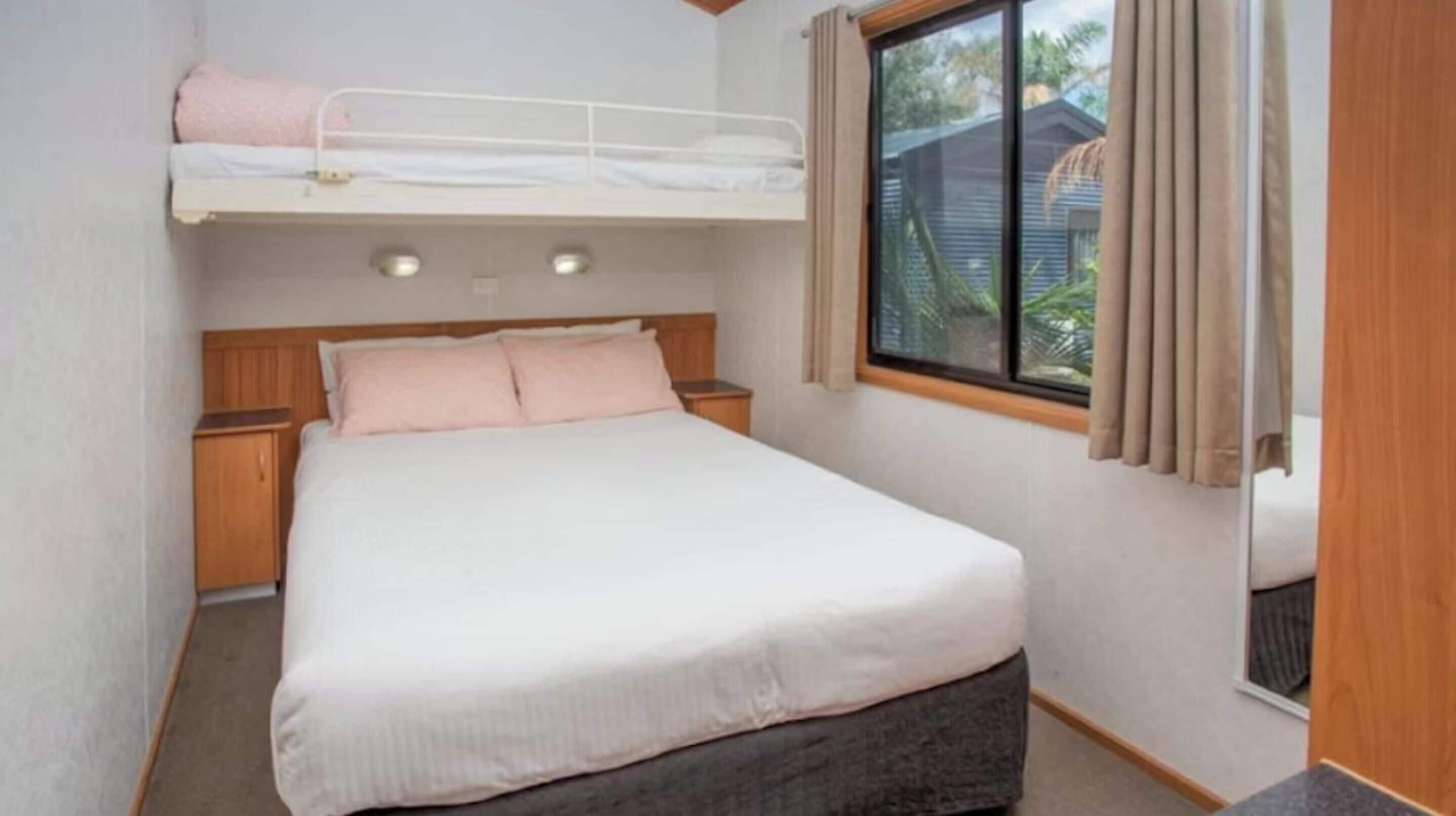 Un dormitorio con una cama litera, una cama individual, cabecero de madera, mesitas de noche y una ventana con cortinas.