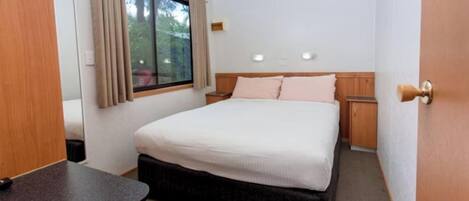A bedroom with a bed, bedside tables, a window with curtains, and a door.