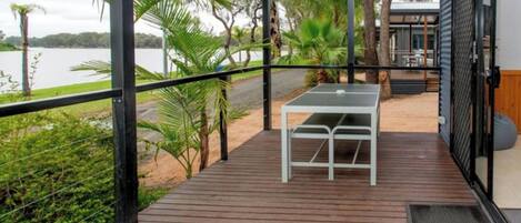 Terraza de madera con mesa y sillas, con vista a un cuerpo de agua rodeado de vegetación.