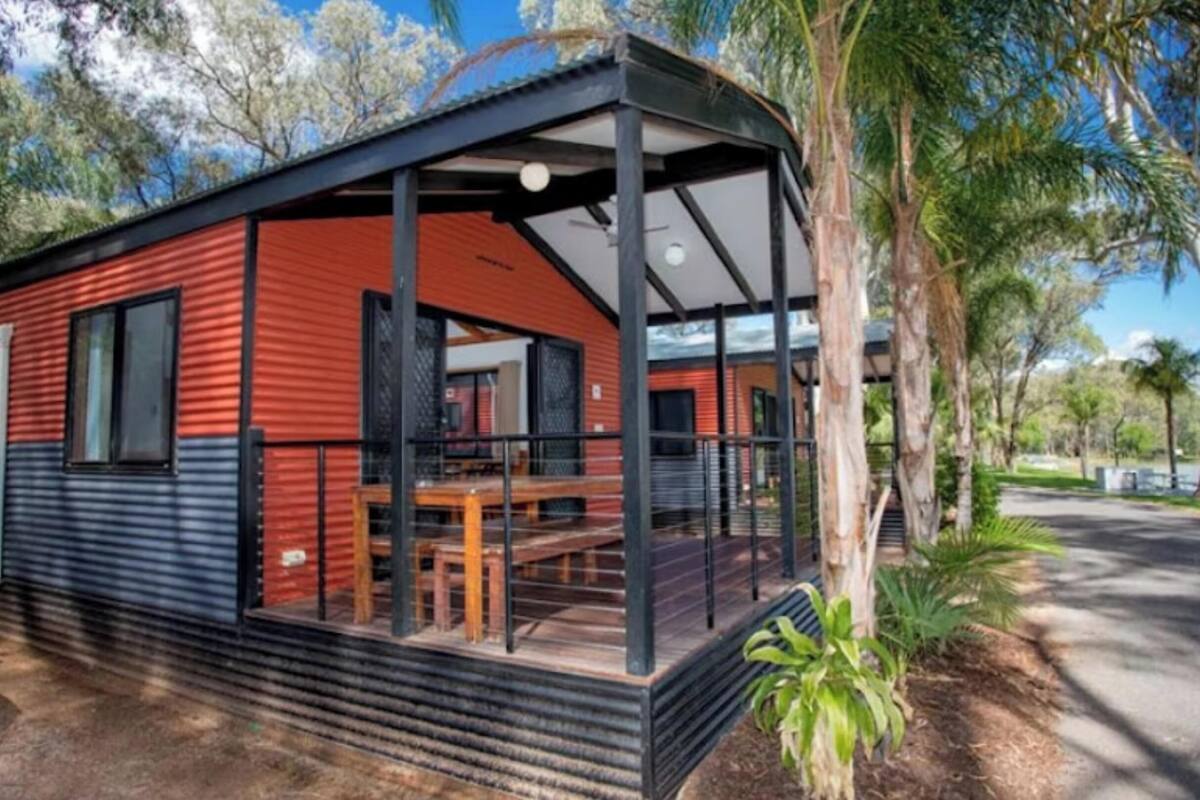Una cabaña con porche cubierto, terraza de madera y vista a un lago.