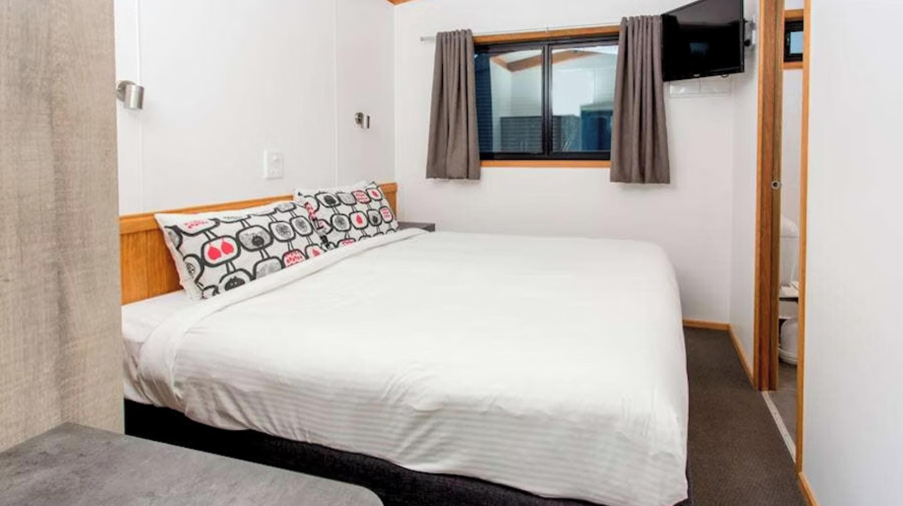 A single-bed room with a wooden headboard, white bedding, and a patterned pillow.
