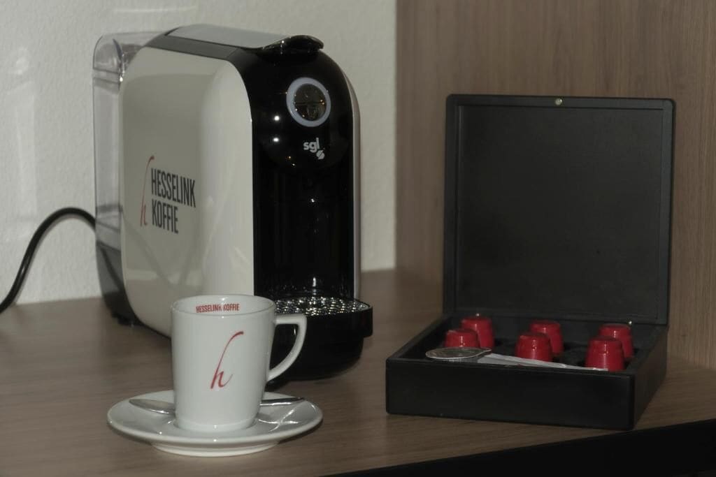 A coffee maker, a cup, and a box of coffee capsules on a table.